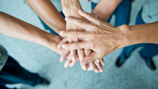 Übereinander gelegte Hände mehrerer Personen als Versinnbildlichung von Zusammenarbeit.