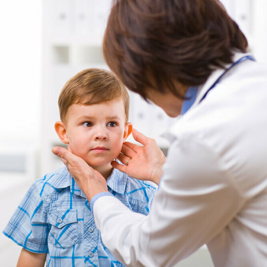 Das Bild zeigt die Rückansicht einer Ärztin, die gerade einen kleinen Jungen medizinisch untersucht. 