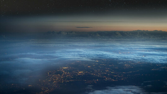 Luftansicht aus großer Höhe durch die Wolken auf eine beleuchtete Stadt.
