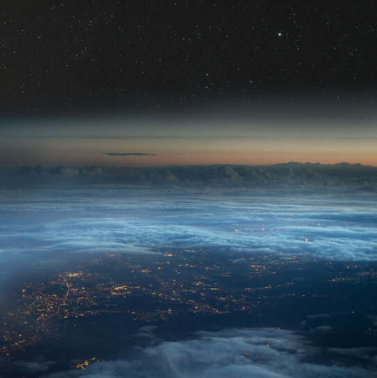 Luftansicht aus großer Höhe durch die Wolken auf eine beleuchtete Stadt.