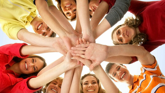Eine Gruppe von menschen steht in einem Kreis und alle Hände treffen sich in der Mitte