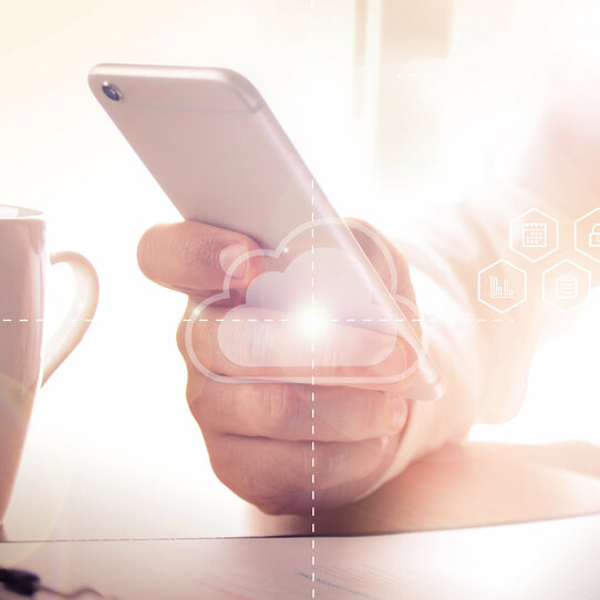 Mann benutzt ein Smartphone ergänzt um Cloud-Icons Ein Mann hält ein Smartphone in der Hand, vor ihm steht ein Tasse Kaffee