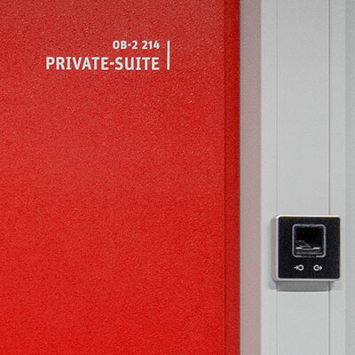 Das Bild zeigt eine rote Sicherheitstür im KAMP-Rechenzentrum. Daneben befindet sich der Fingerabdruckscanner für die biometrische Zutrittskontrolle. 