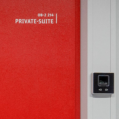 Eingang zur KAMP Private-Suite mit biometrischer Zutrittskontrolle Das Bild zeigt eine rote Sicherheitstür im KAMP-Rechenzentrum. Daneben befindet sich der Fingerabdruckscanner für die biometrische Zutrittskontrolle.