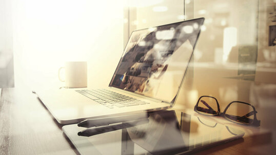 Büroarbeitsplatz mit Laptop, Tablet Brille und Stift auf einem Schreibtisch mit unscharfem Hintergrund.
