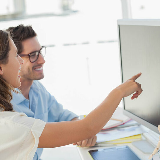 Zwei Personen vor einem Monitor Zwei Personen, ein Mann und eine Frau, betrachten etwas am Monitor. Die Frau weist den Mann auf etwas hin.