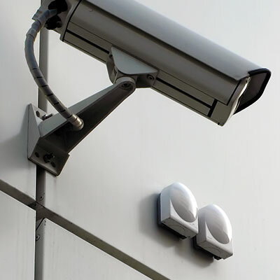Das Bild zeigt eine auf einer hellen Gebäudewand angebrachte Sicherheitskamera.