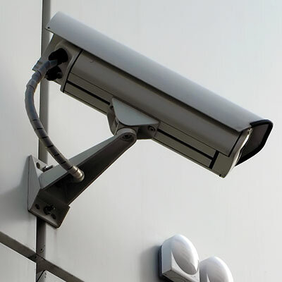 Das Bild zeigt eine auf einer hellen Gebäudewand angebrachte Sicherheitskamera.