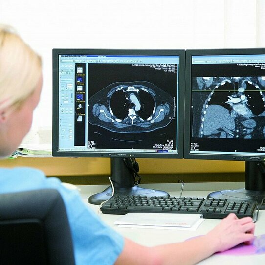 Eine Frau betrachtet auf zwei Monitoren die Ergebnisse der bildgebenden Diagnostik.