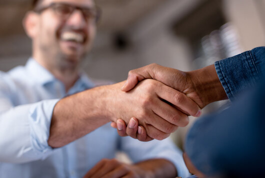 Handshake zwischen zwei Personen, eine davon lacht