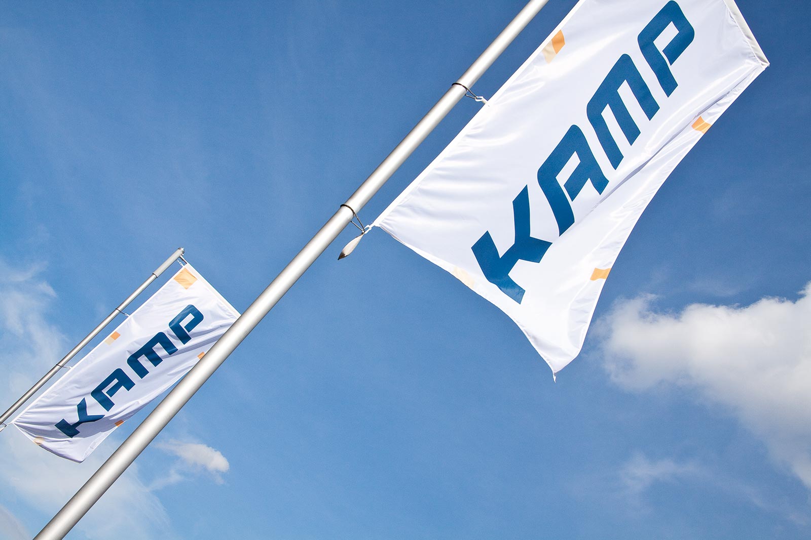 KAMP Fahnen vor blauem Himmel Das Bild zeigt die Fahnenmasten vor dem KAMP Betriebsgelände vor blauem Himmel