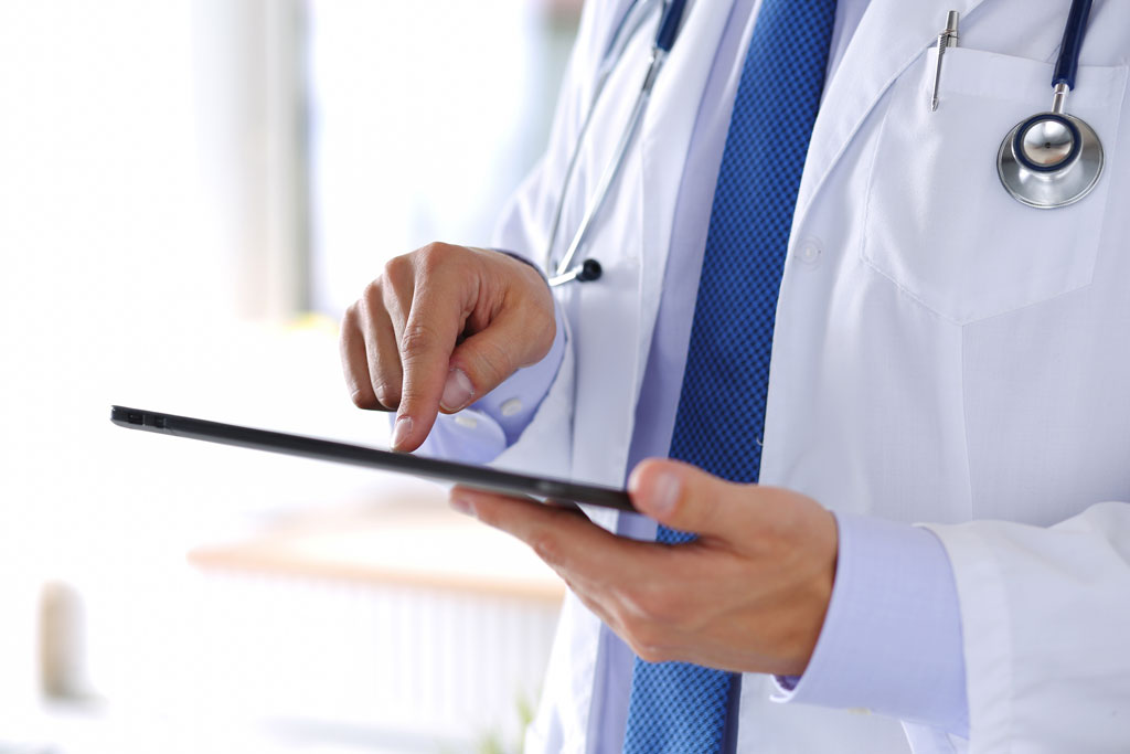 Arzt mit Tablet Ausschnittsweise Darstellung eines Arztes mit Kittel und Stethoskop, der an einem Tablet arbeitet.